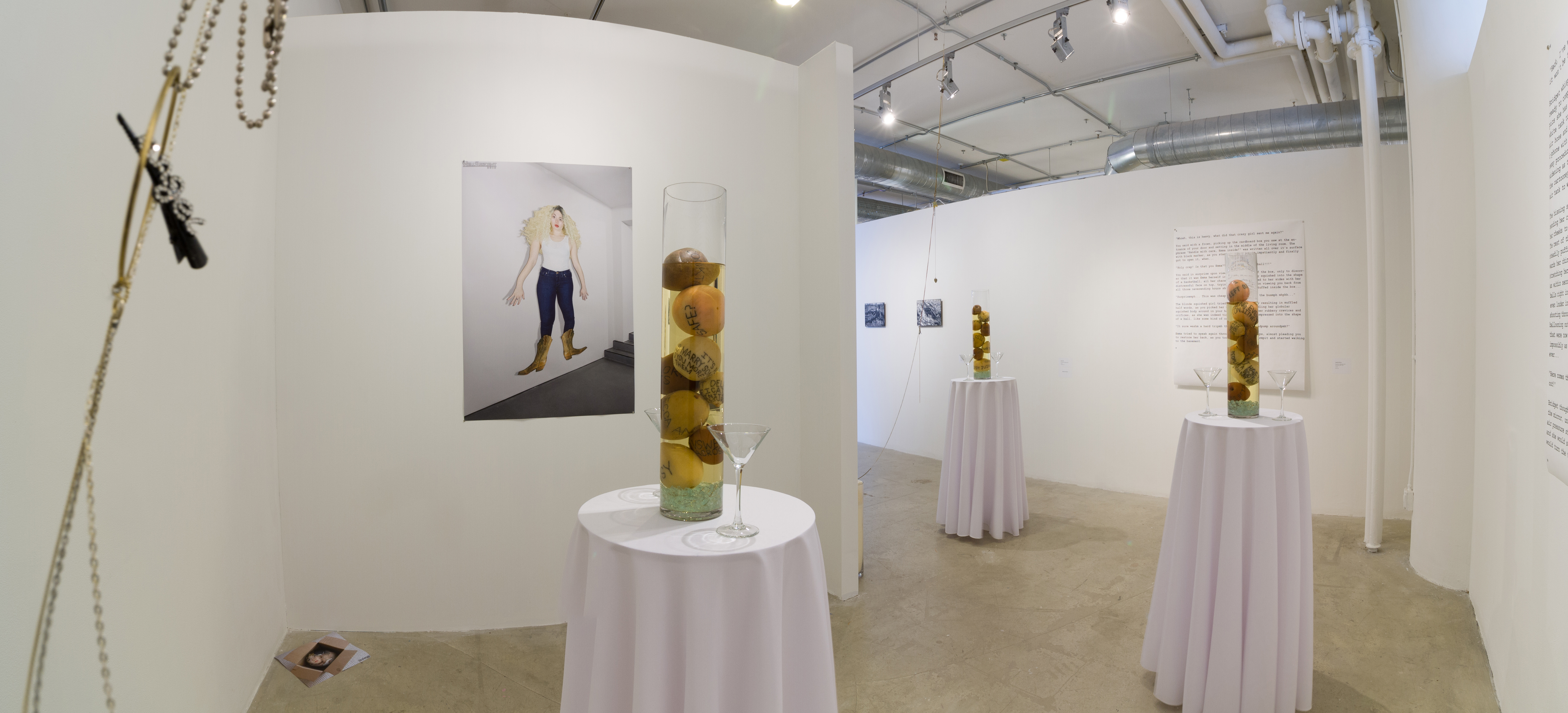 Installation view of three round tables with fruit colums on them and various prints in a white wall gallery